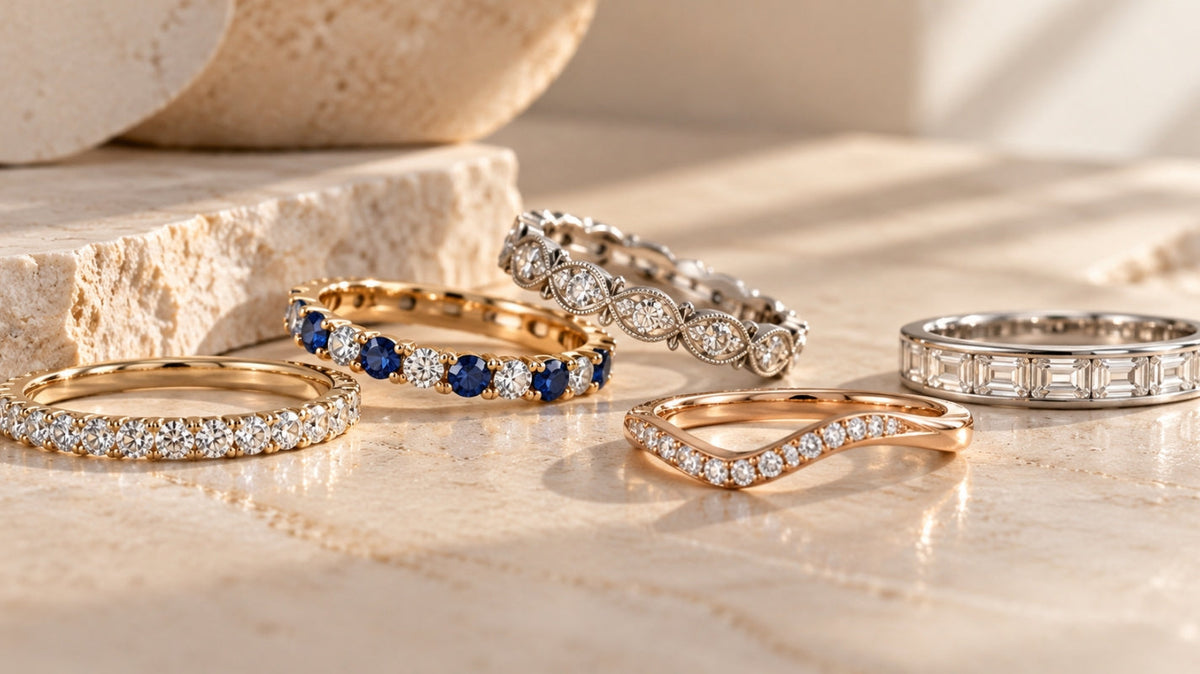 Curated collection of five luxury wedding bands featuring diamond, sapphire, vintage, curved, and baguette designs on a warm stone surface.