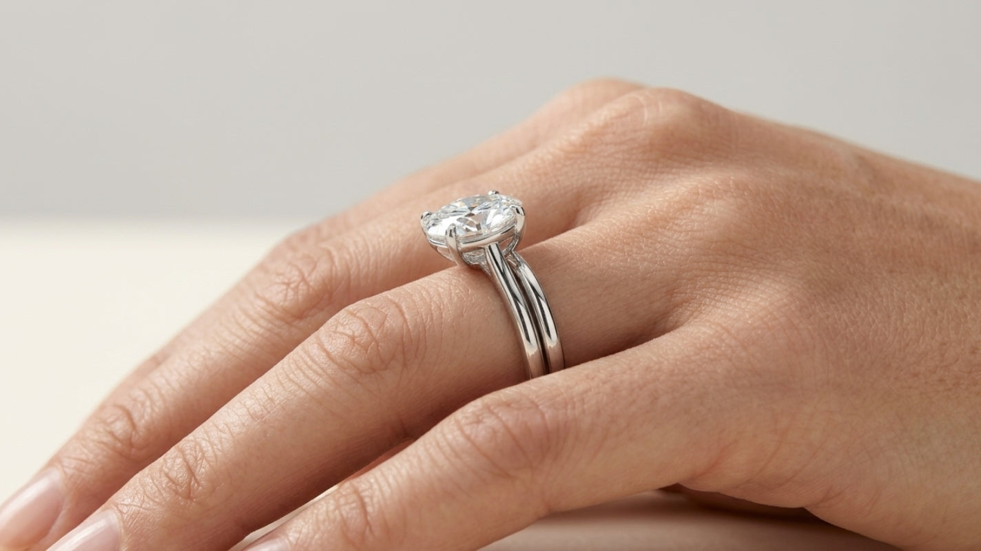 Close-up of a hand wearing a low-profile oval moissanite solitaire in a polished white-metal setting, shown from the side to reveal its compact basket height.