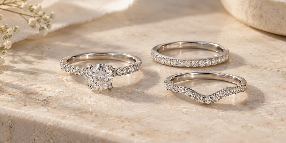 Diamond engagement ring displayed with straight and contoured wedding band options on a soft ivory stone surface.