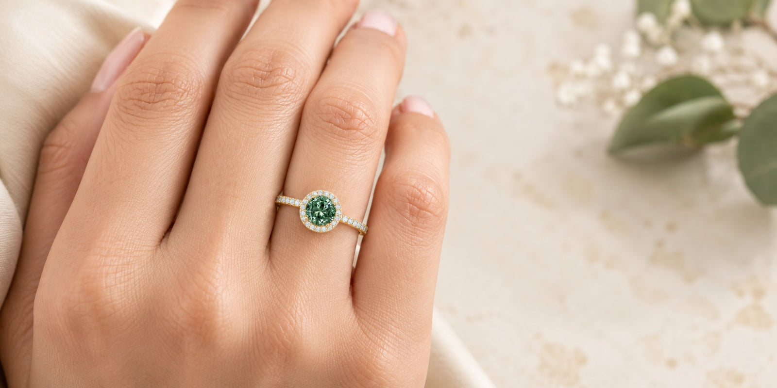 Hand wearing a yellow gold halo engagement ring with a round lab-grown green diamond