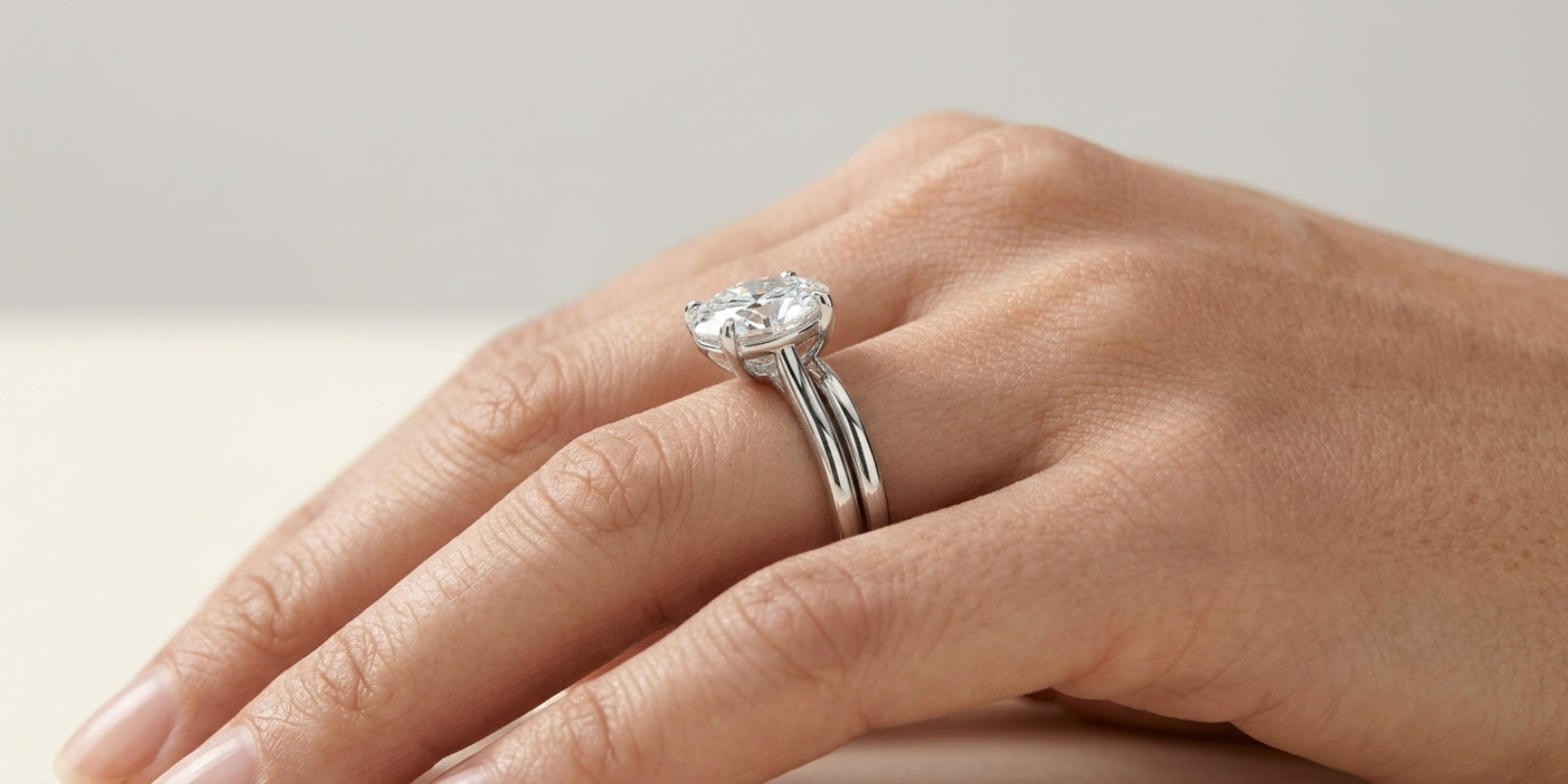 Close-up of a hand wearing a low-profile oval moissanite solitaire in a polished white-metal setting, shown from the side to reveal its compact basket height.